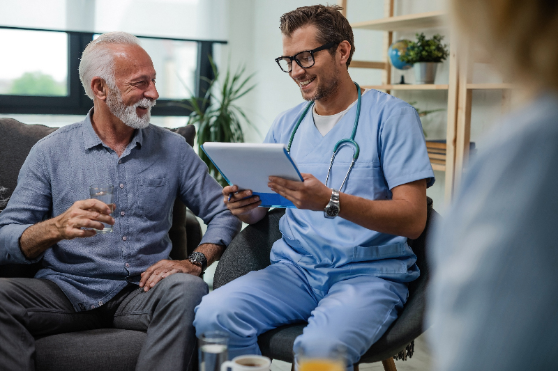 Healthcare professional sitting with a man reviewing information on a tablet.